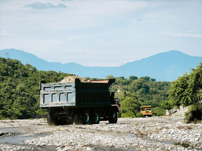 Dump truck on rocky riverbed with green trees and blue mountains in the background