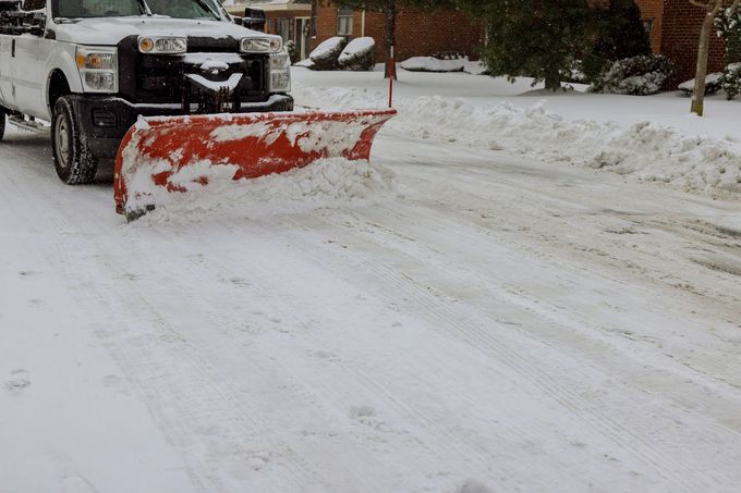 Snowplow clearing a snowy residential street, with a pickup truck behind it