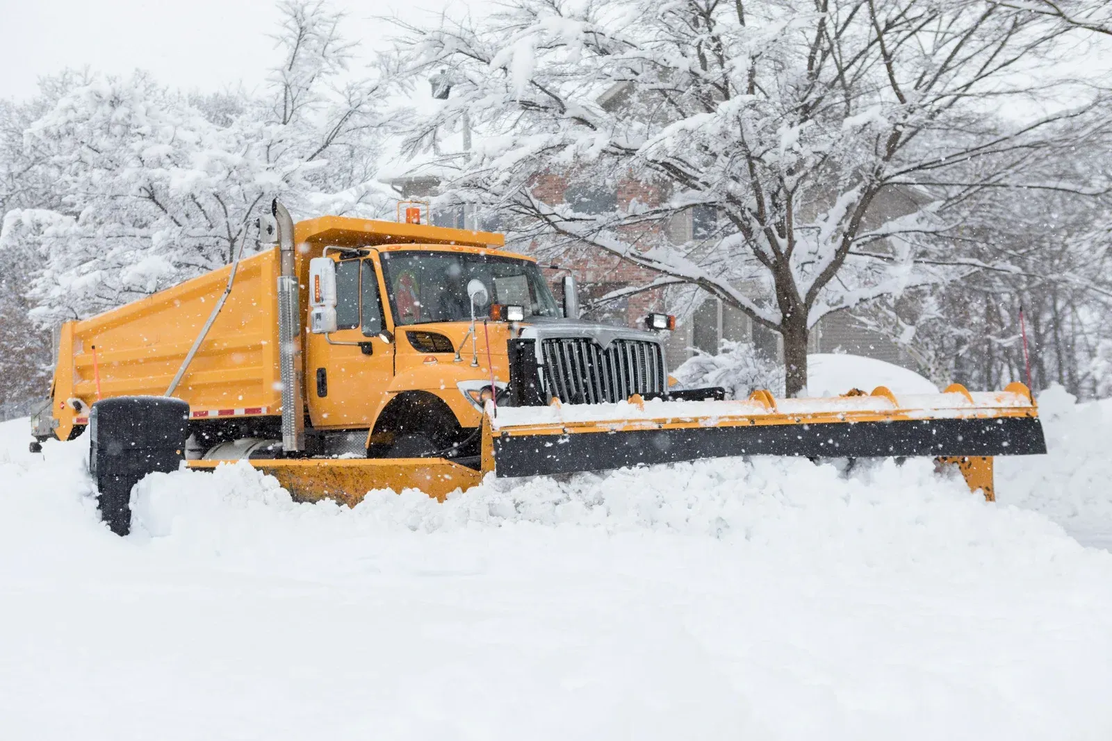 Yellow snowplow clearing deep snow on a road in a winter landscape