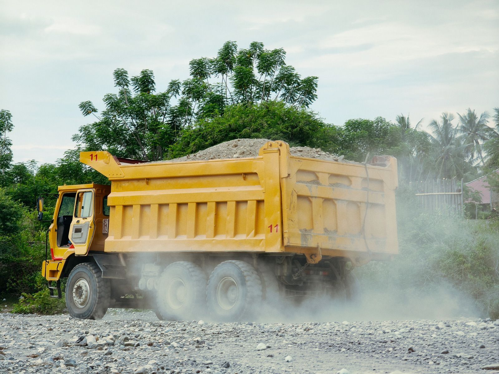 Yellow dump truck driving on a dusty gravel road with dust cloud behind it