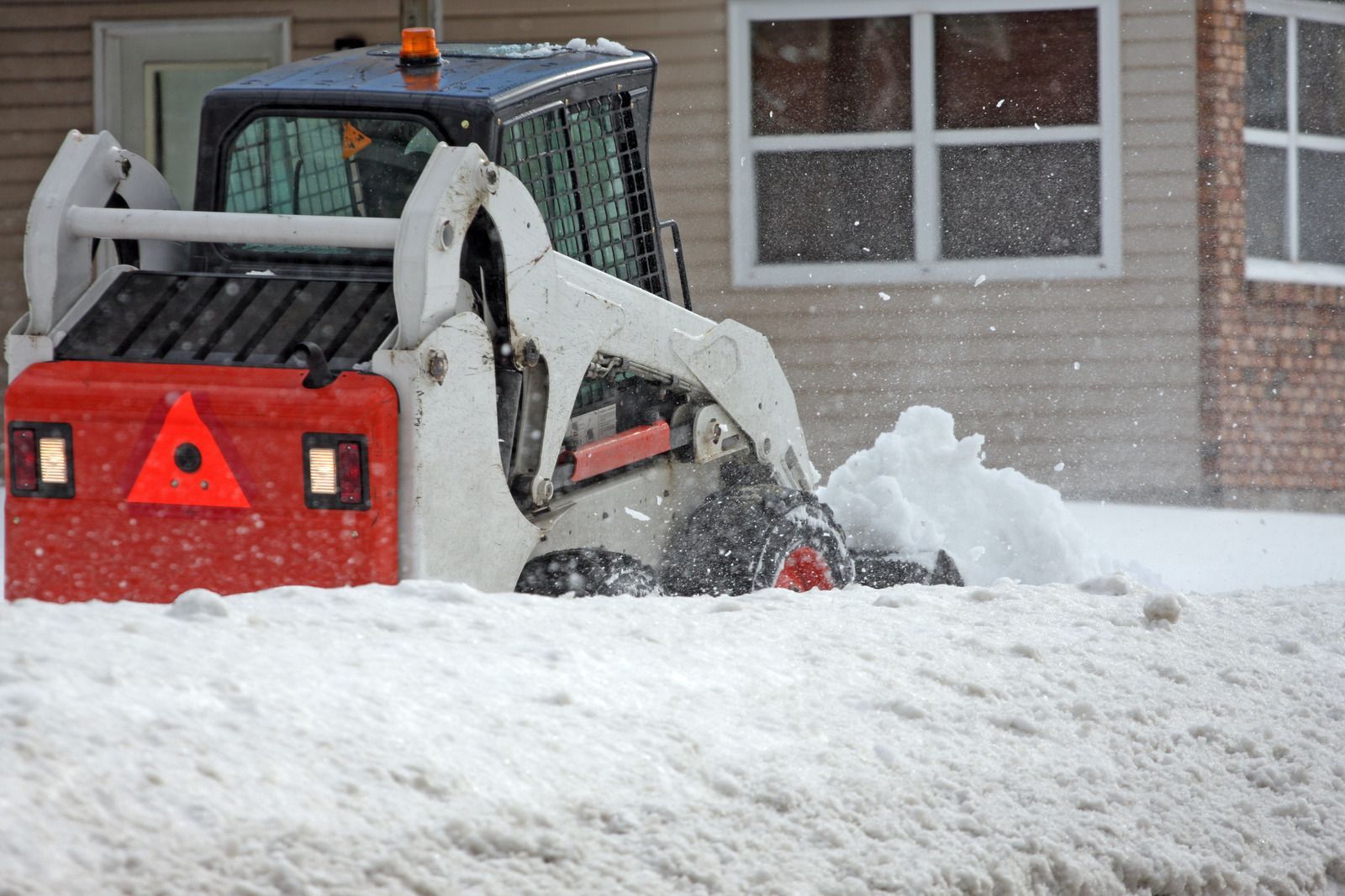 Skid steer clearing deep snow outside a house during a snowstorm
