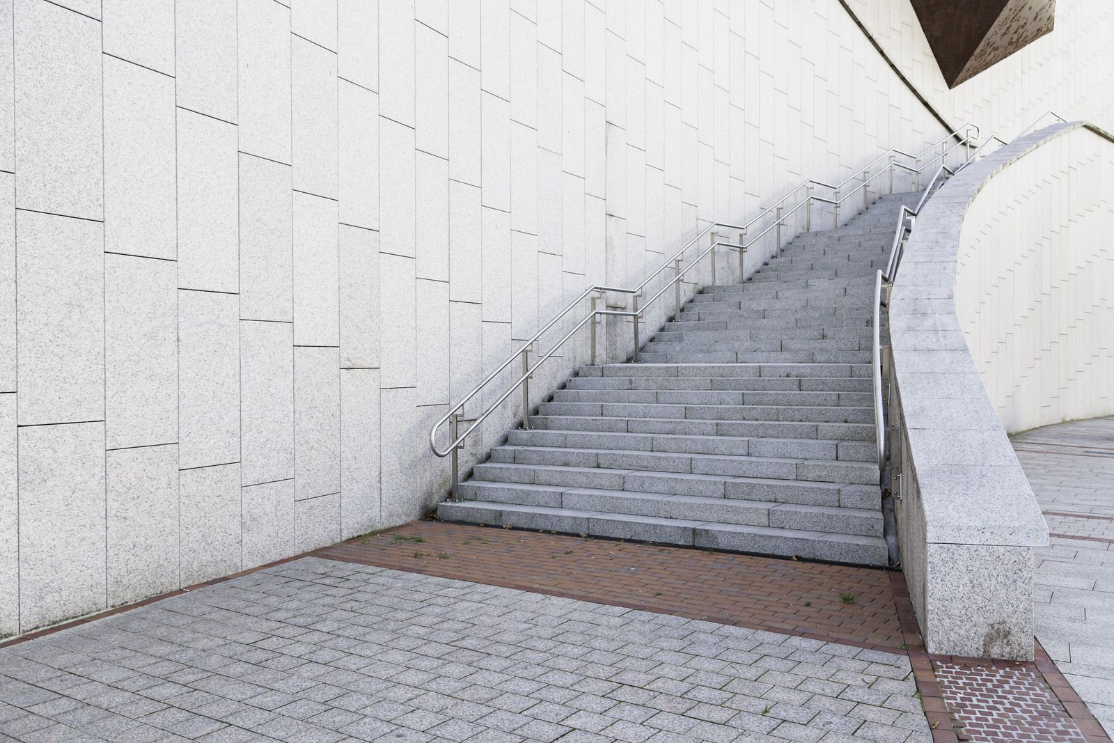 Curved concrete stairway beside a white tiled wall and paved walkway outdoors