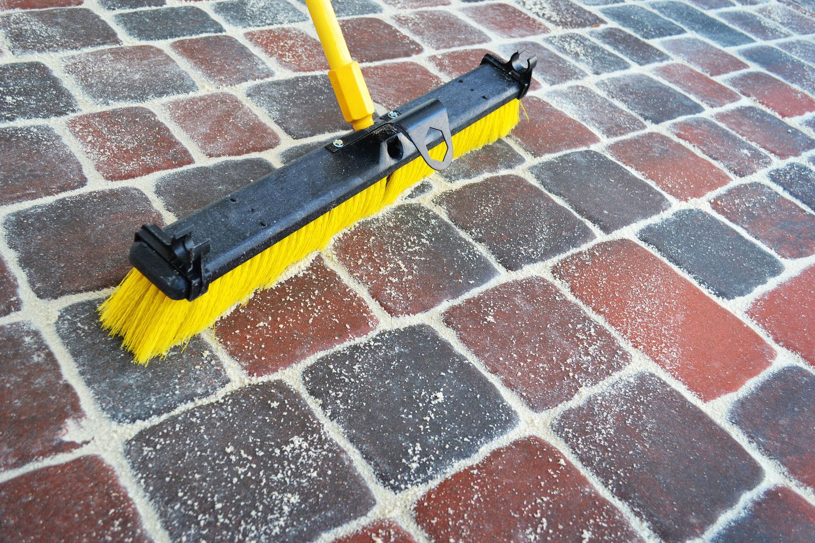 Yellow broom cleaning brick pavement with scattered white debris