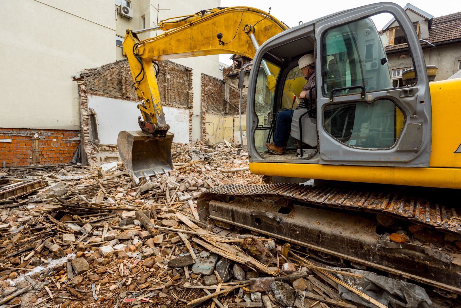 Yellow excavator clearing rubble beside a brick wall at a demolition site