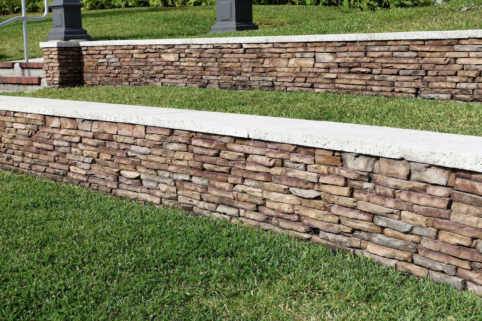 Curved stone retaining walls with white caps beside a green grassy slope in a landscaped park