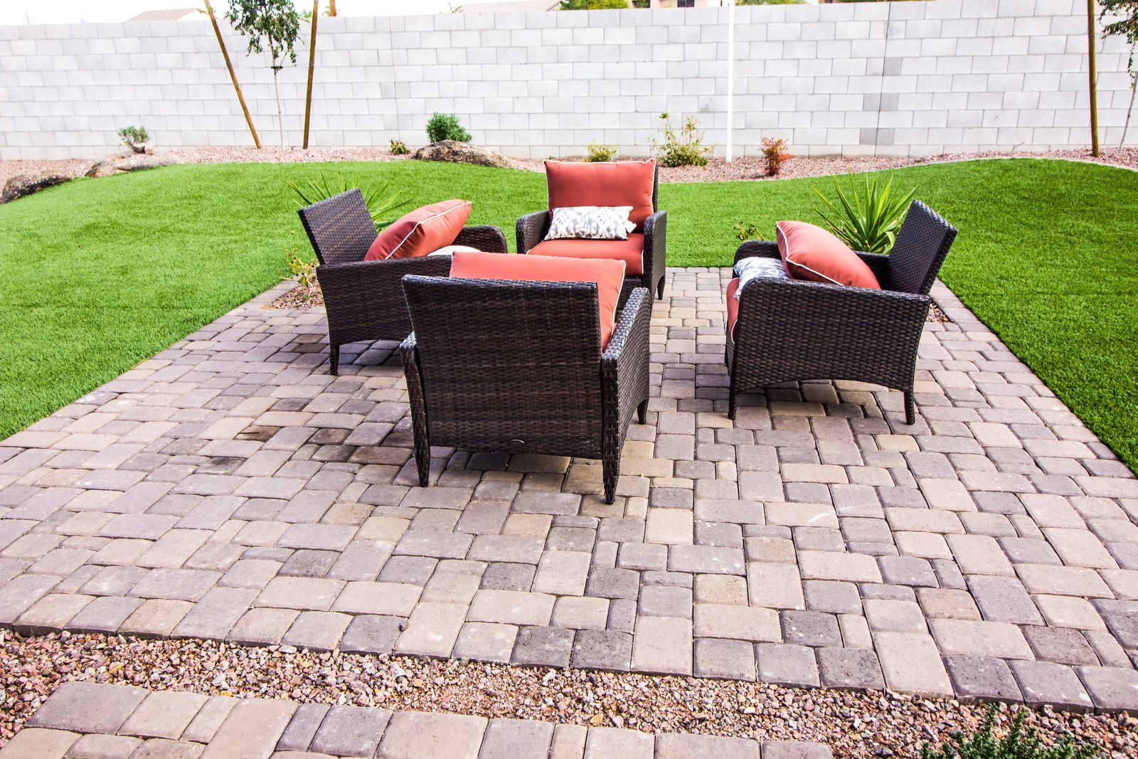 Outdoor patio with dark wicker chairs and orange cushions on a stone paver площадка in a grassy backyard