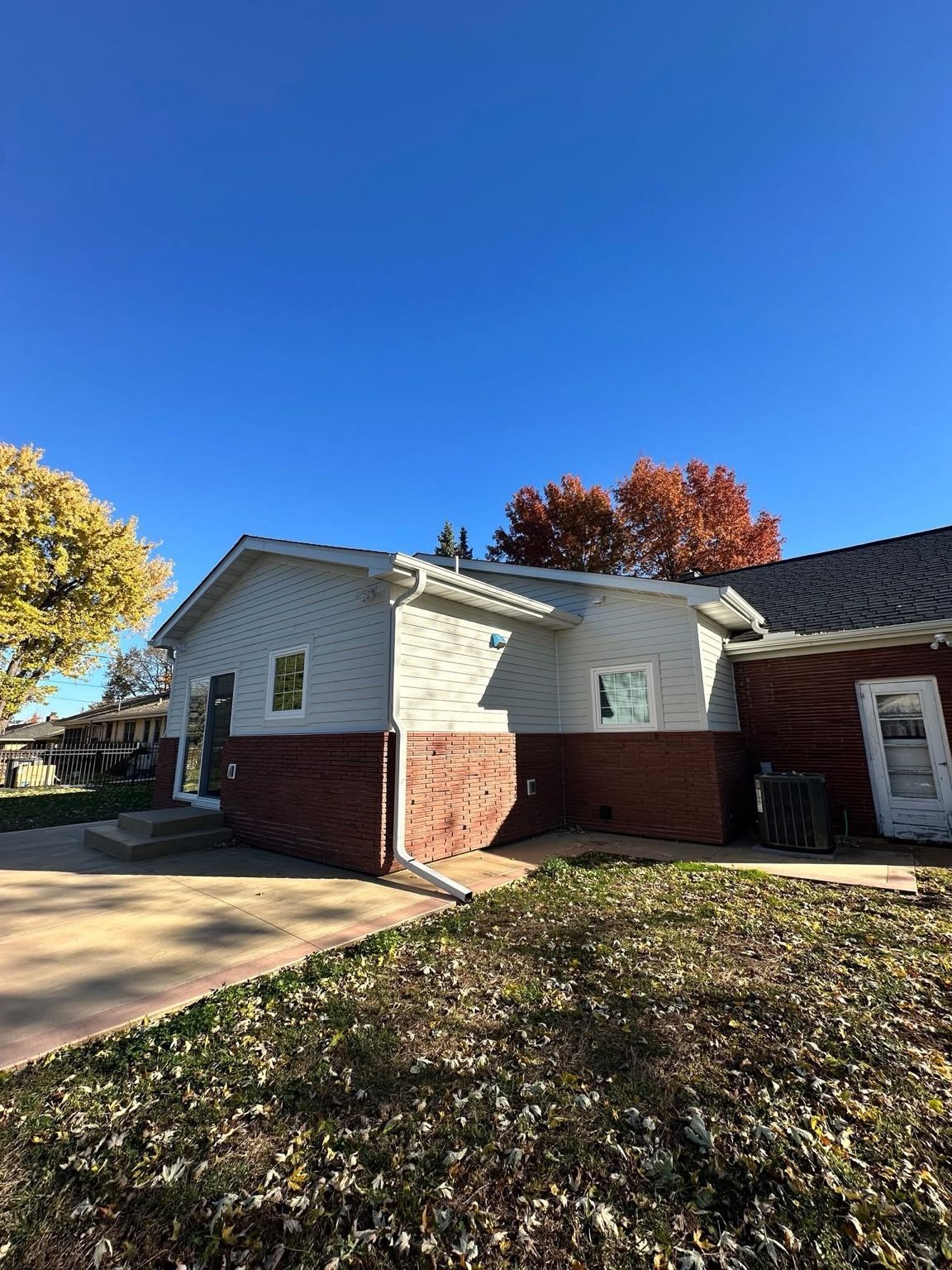 Brick-and-white suburban house with a driveway, autumn trees, and a clear blue sky