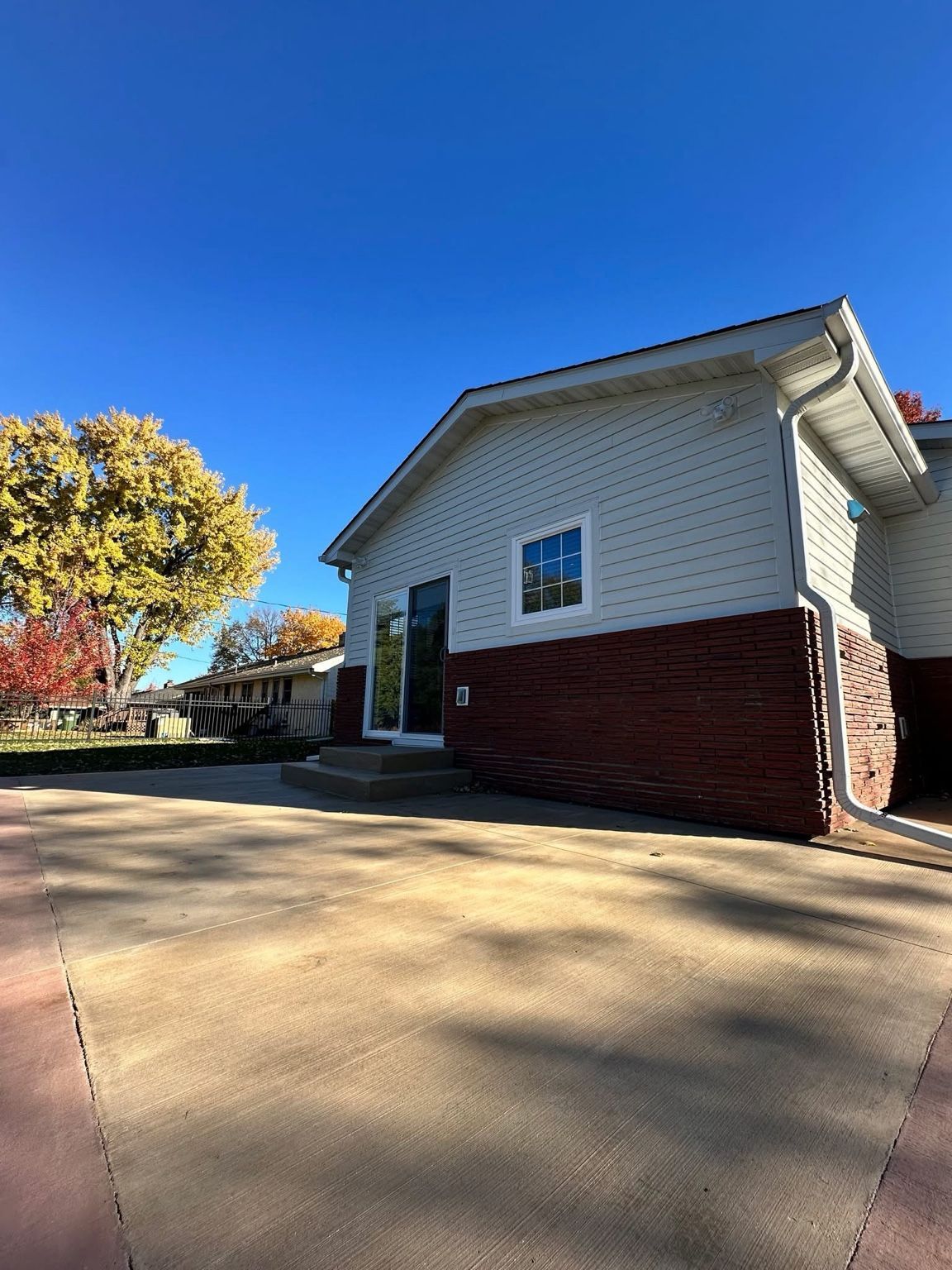 White and red house exterior with a concrete driveway under a clear blue sky