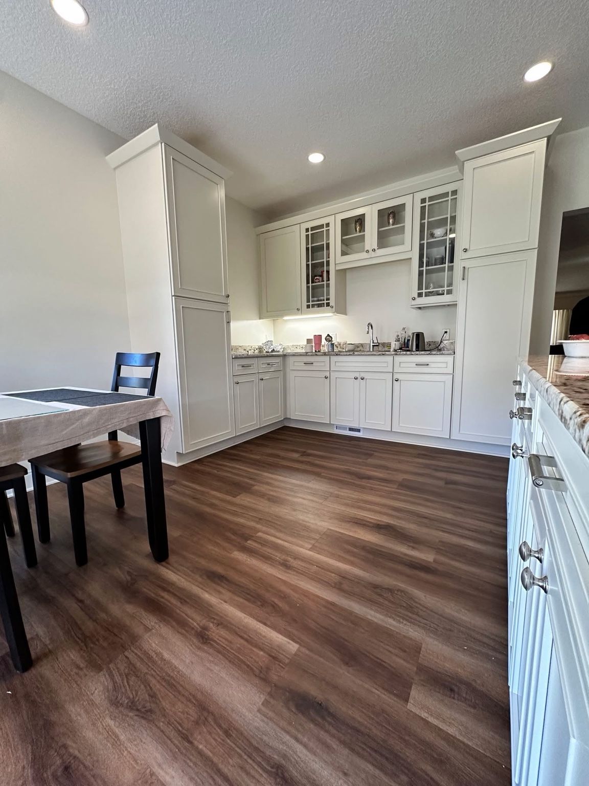 Bright kitchen with white cabinets, wood floors, and a dining table in the foreground