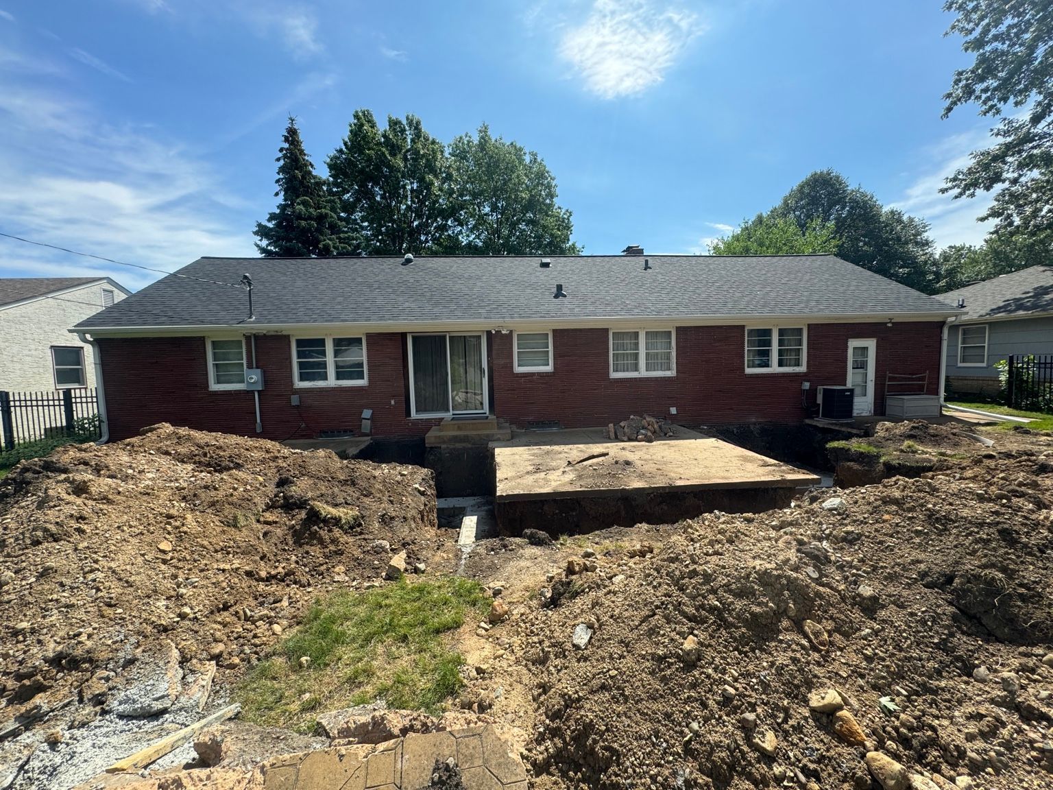 Single-story brick house with excavated front yard and dirt piles under a blue sky