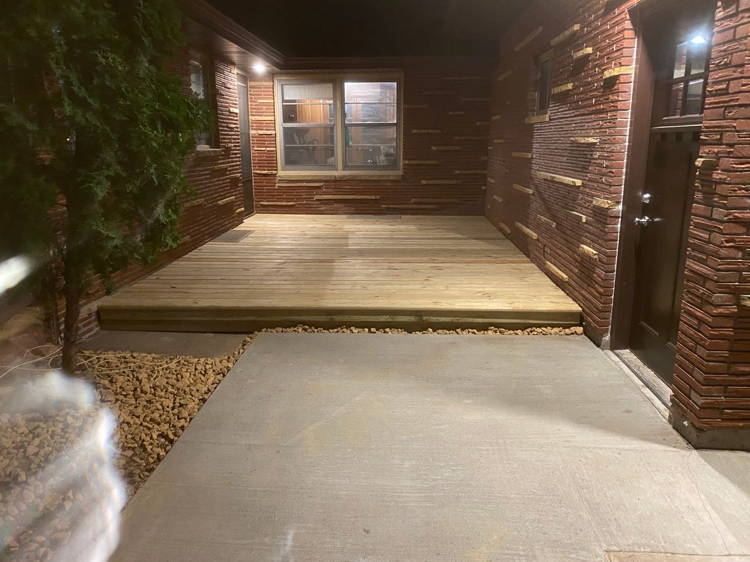 Brick front porch with wooden steps, concrete path, and lit windows at night