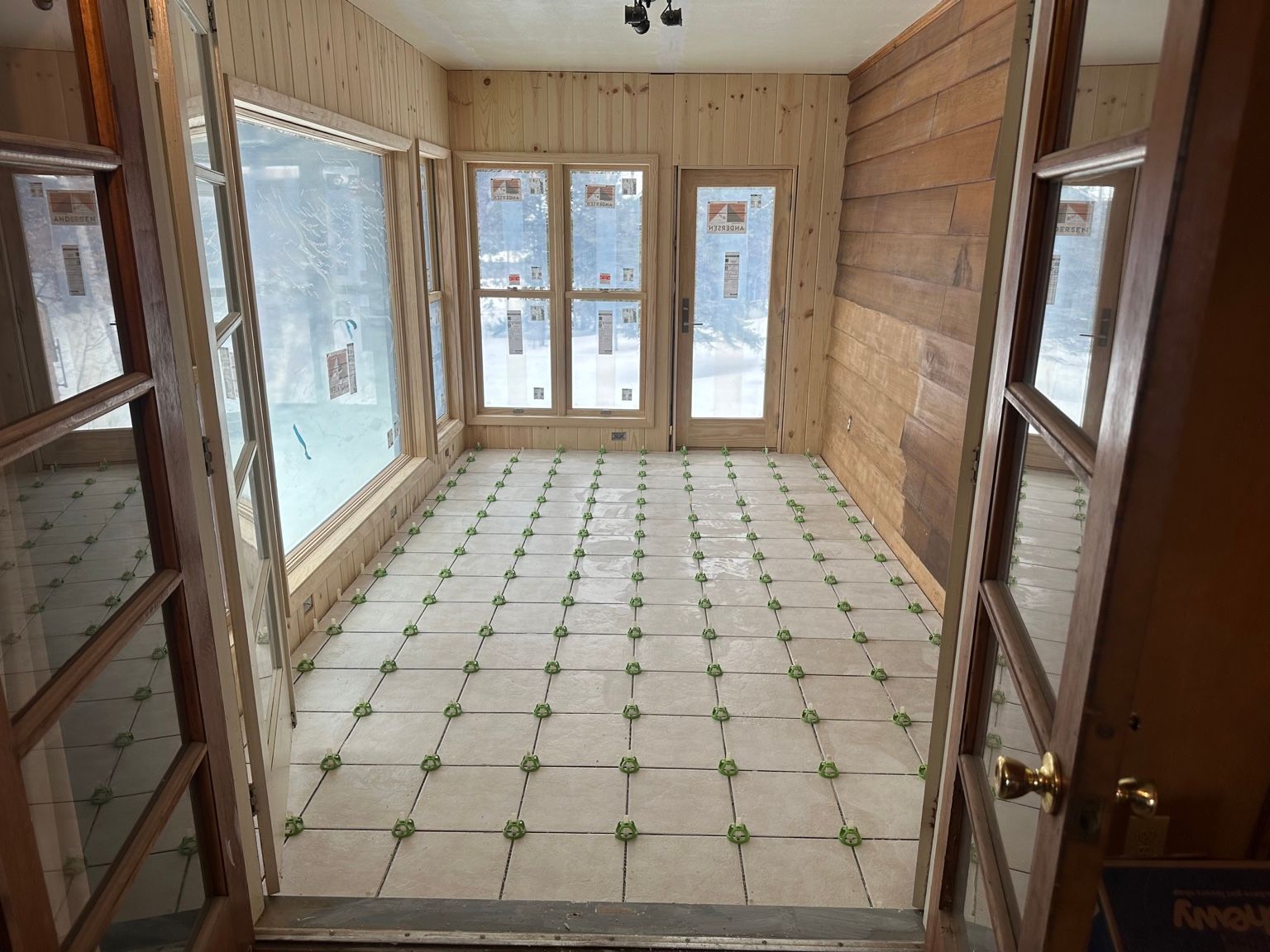 Empty sunroom with wood-paneled walls, tiled floor, and large windows at the far end.