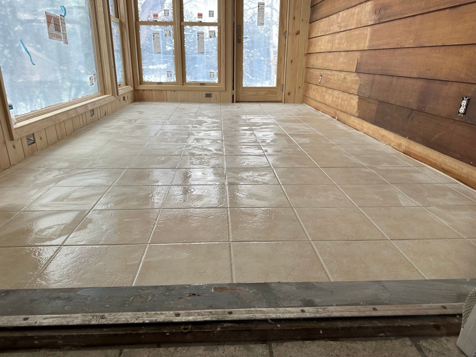 Unfinished room with tiled floor, wood-paneled walls, and glass doors at the far end