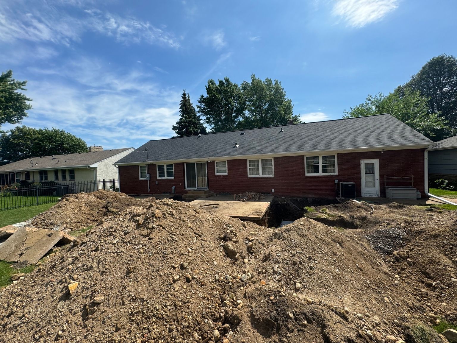 Dirt piles in front of a red single-story house under a blue sky.