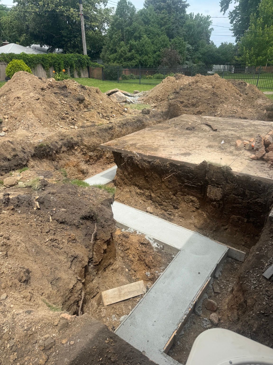 Construction site with excavated foundation trench, concrete footings, and dirt piles.
