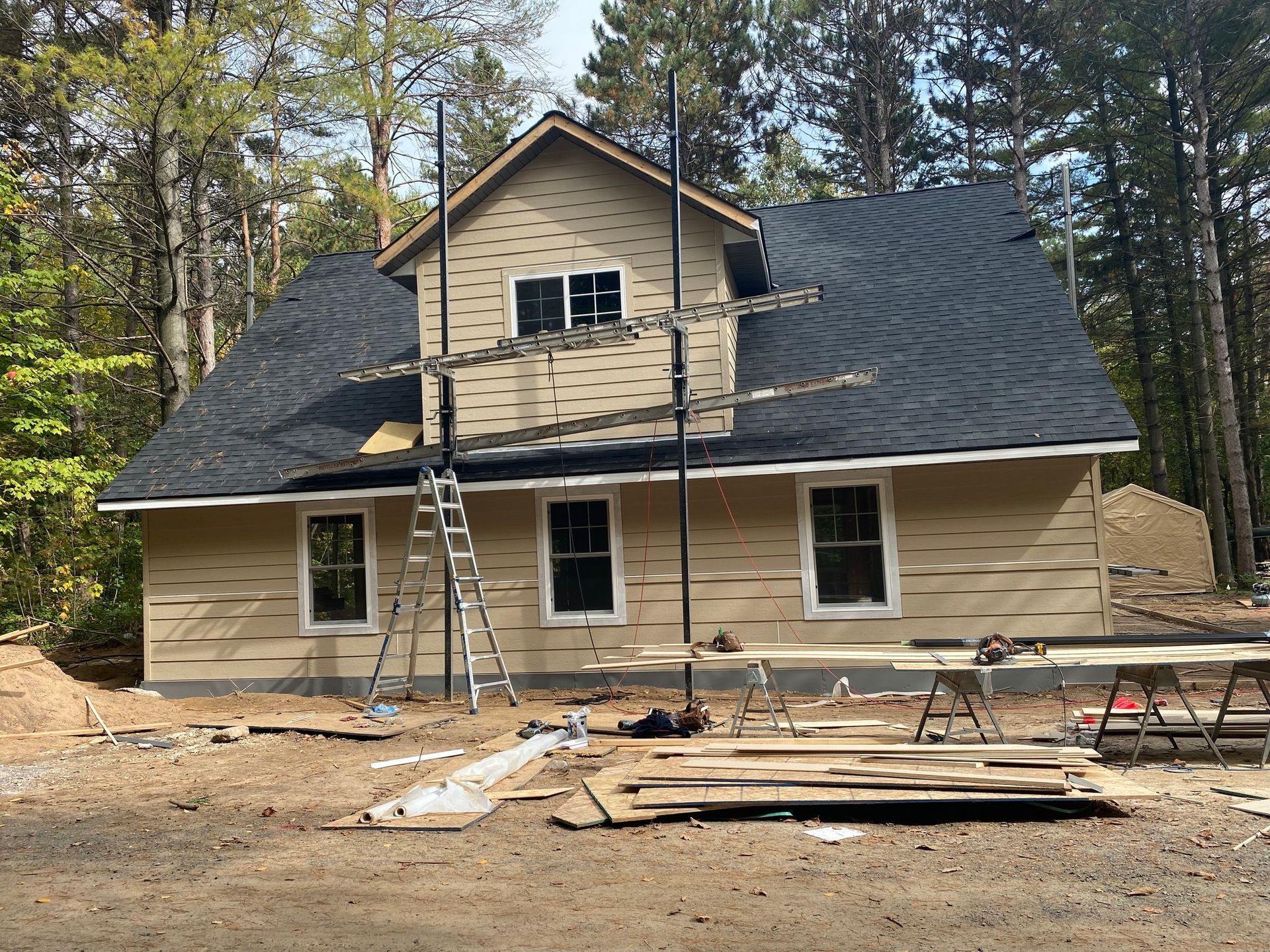 House under construction with roof shingles, ladders, and building materials in front yard