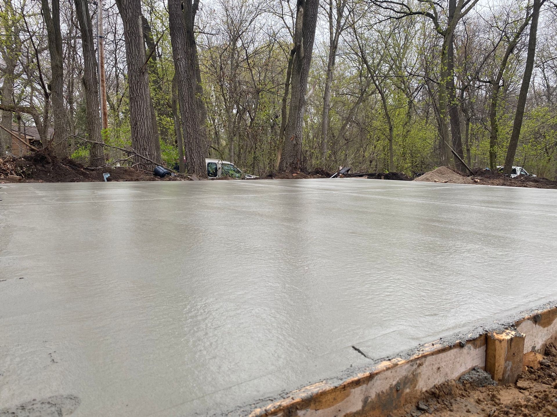 Flooded river beside leafless trees and a muddy bank under gray skies