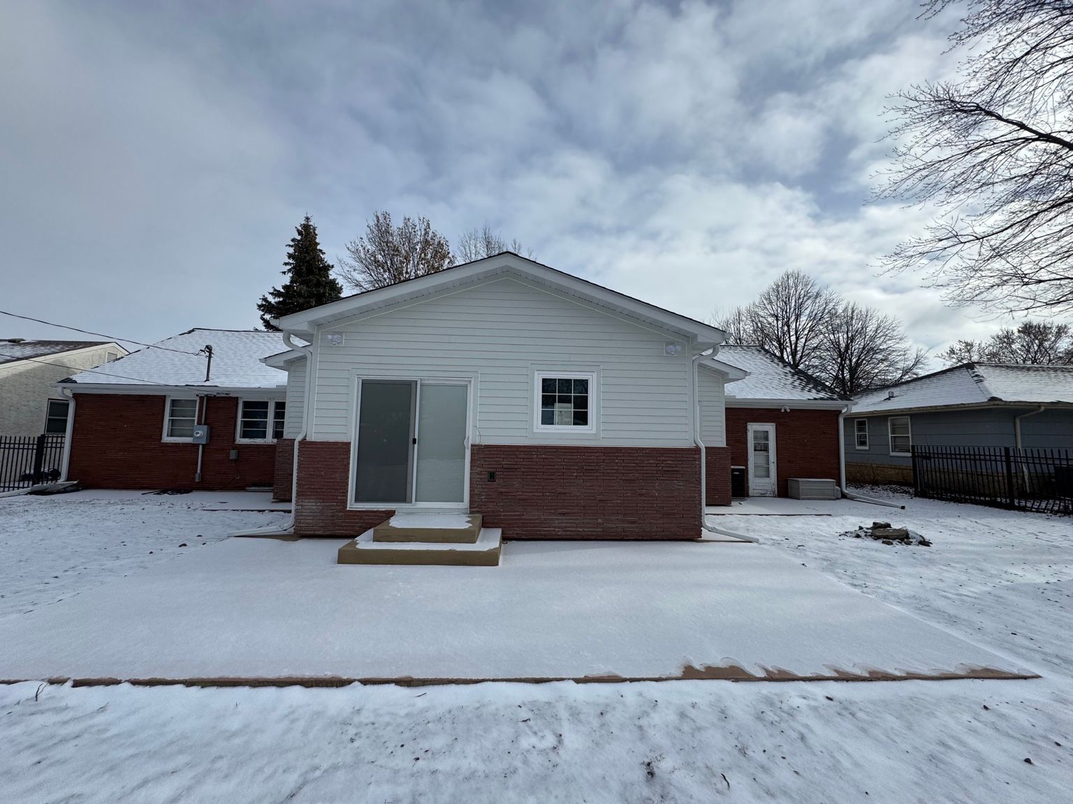 Snow-covered suburban house with white siding, red brick base, and a cloudy winter sky