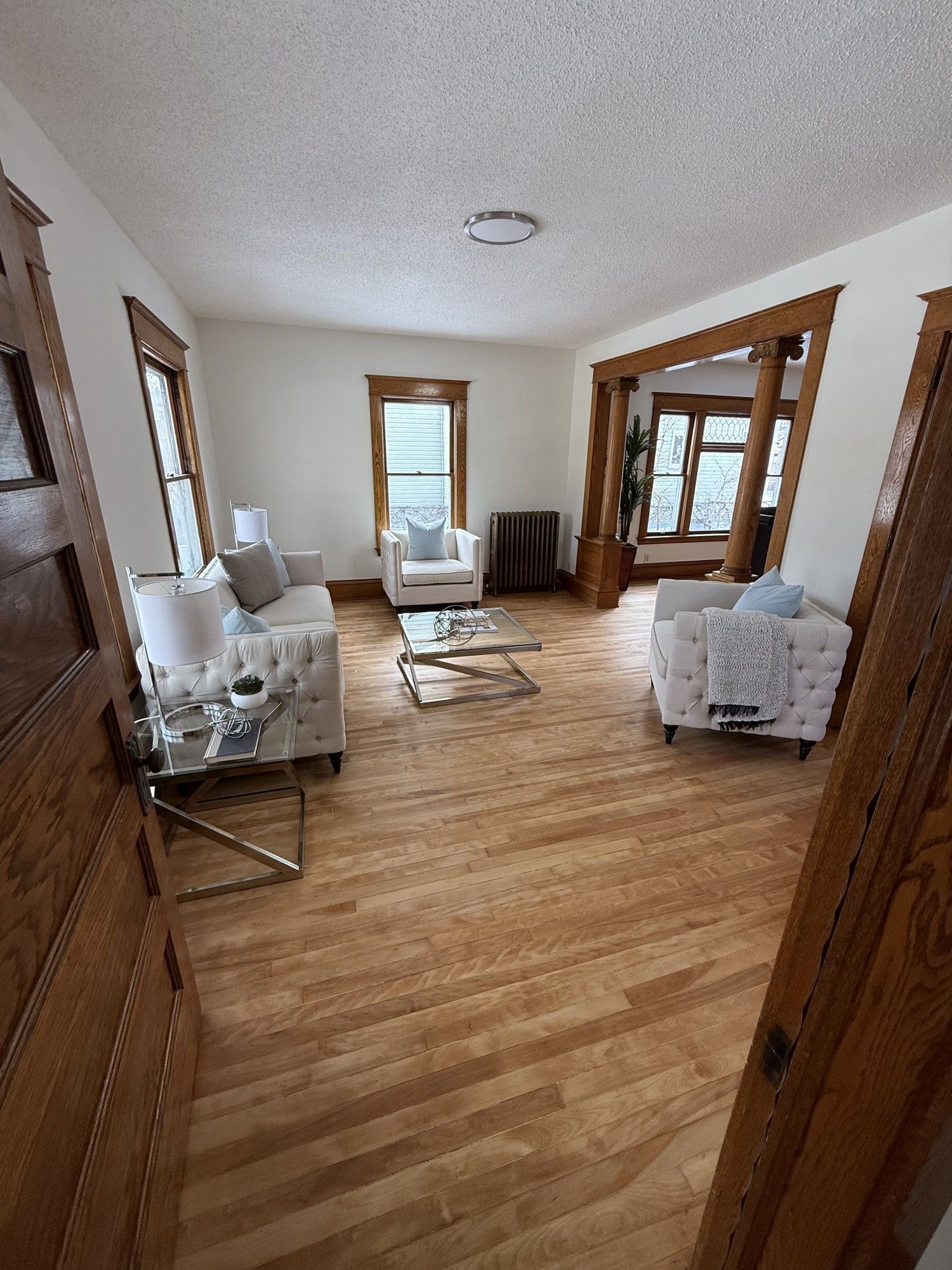 Empty living room with hardwood floors, white walls, and furniture wrapped in protective plastic.