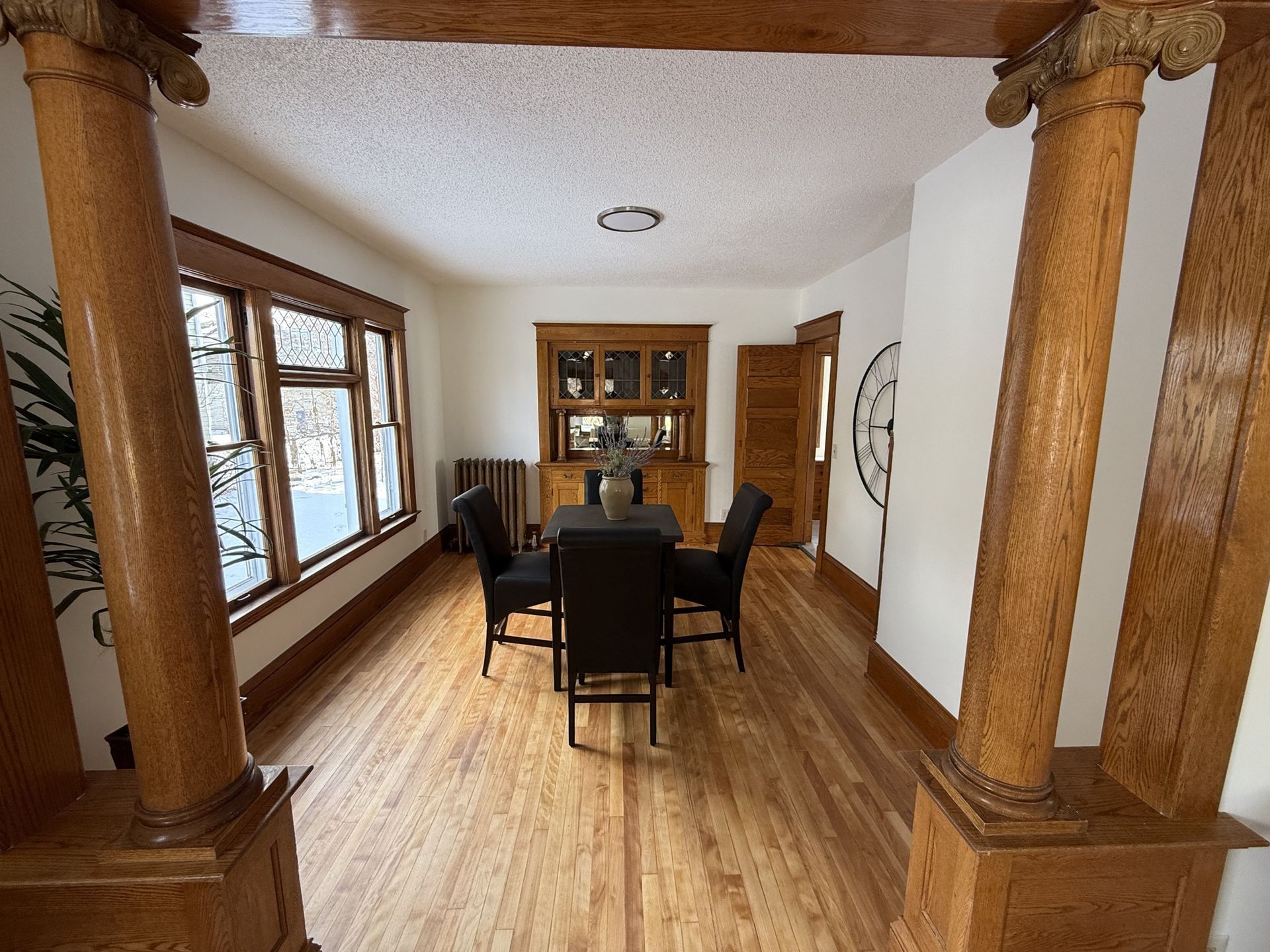 Dining room with wood floors, columns, large windows, and a dark table and chairs centered in the space