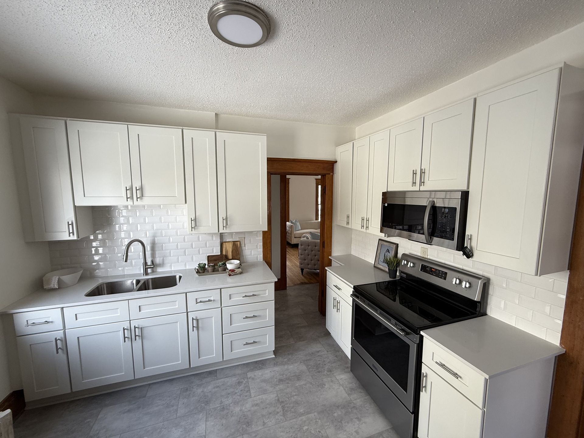 Bright white kitchen with black appliances, gray floor, and wood-trimmed doorway.