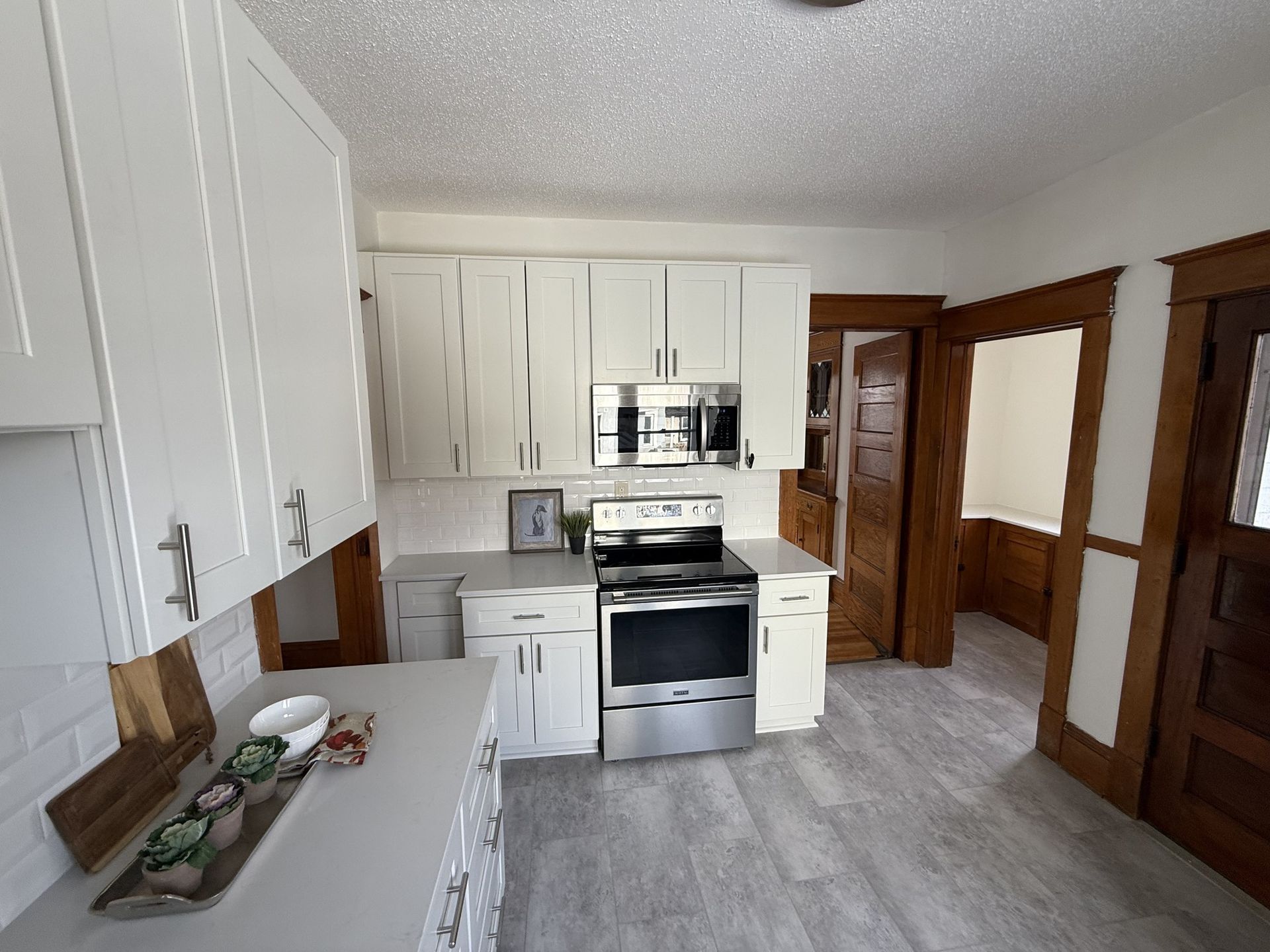 Bright kitchen with white cabinets, stainless appliances, and wood trim on the doors and walls.