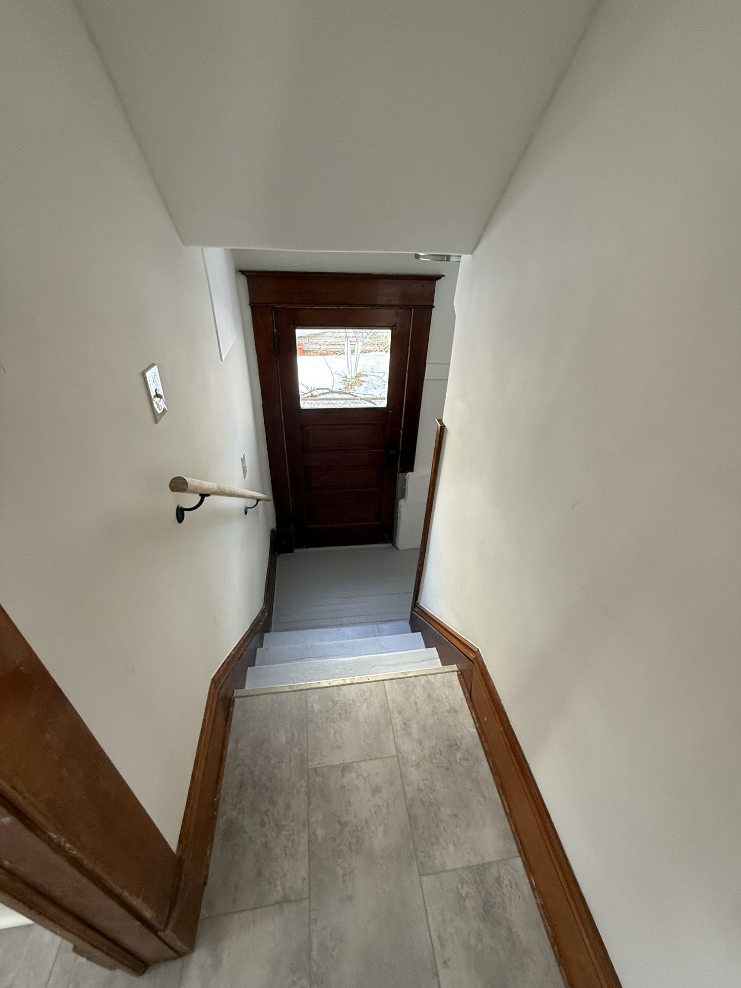 Narrow hallway with stairs leading to a dark wooden front door and a small window.