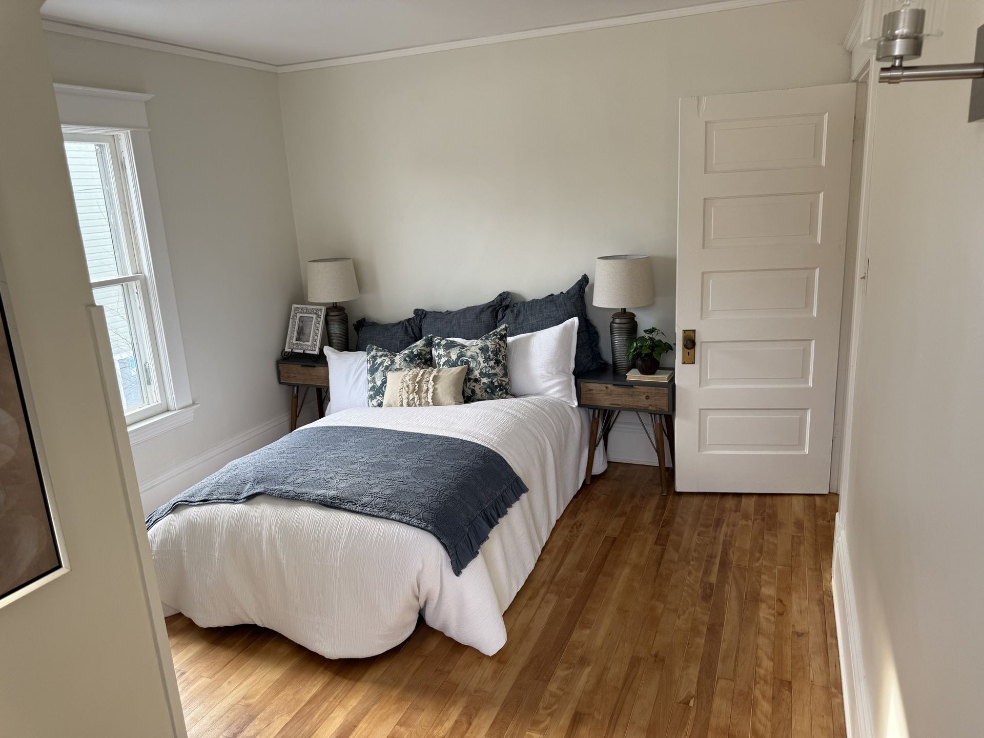 Bright bedroom with a bed, wooden floor, white walls, and a closed door on the right.