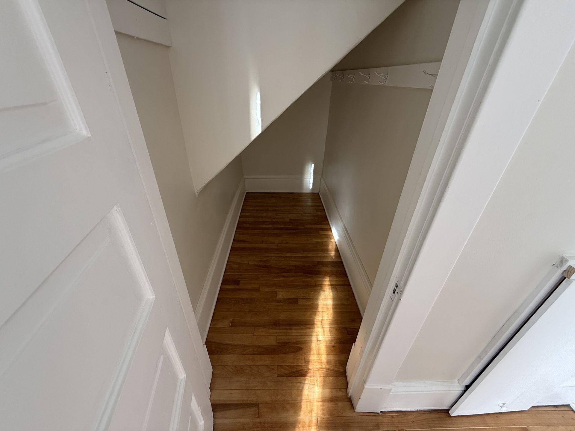 Narrow stairway with wooden steps and white walls under a slanted ceiling