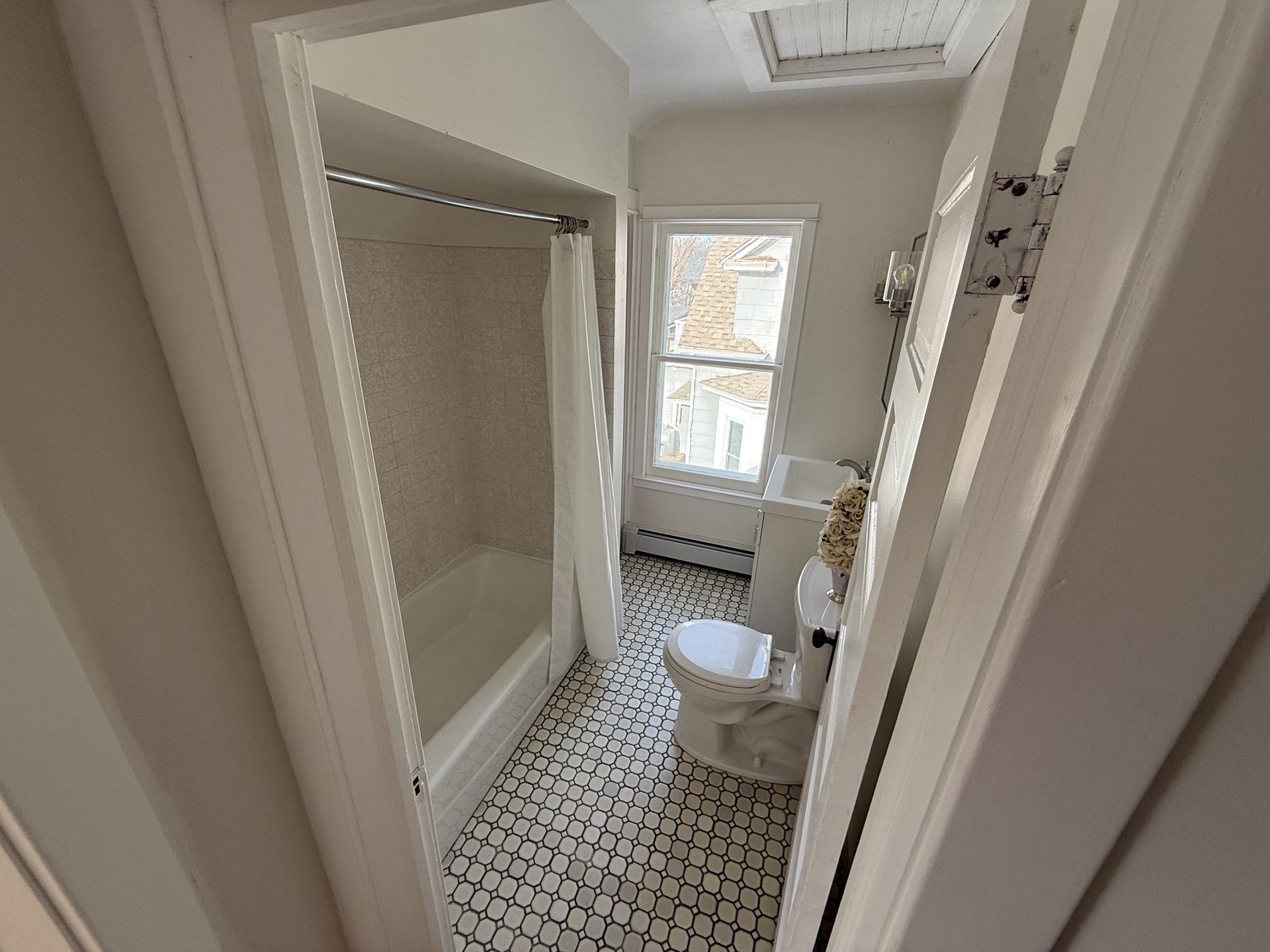 Small bathroom with white tub, toilet, and black-and-white tile floor, viewed from the doorway.