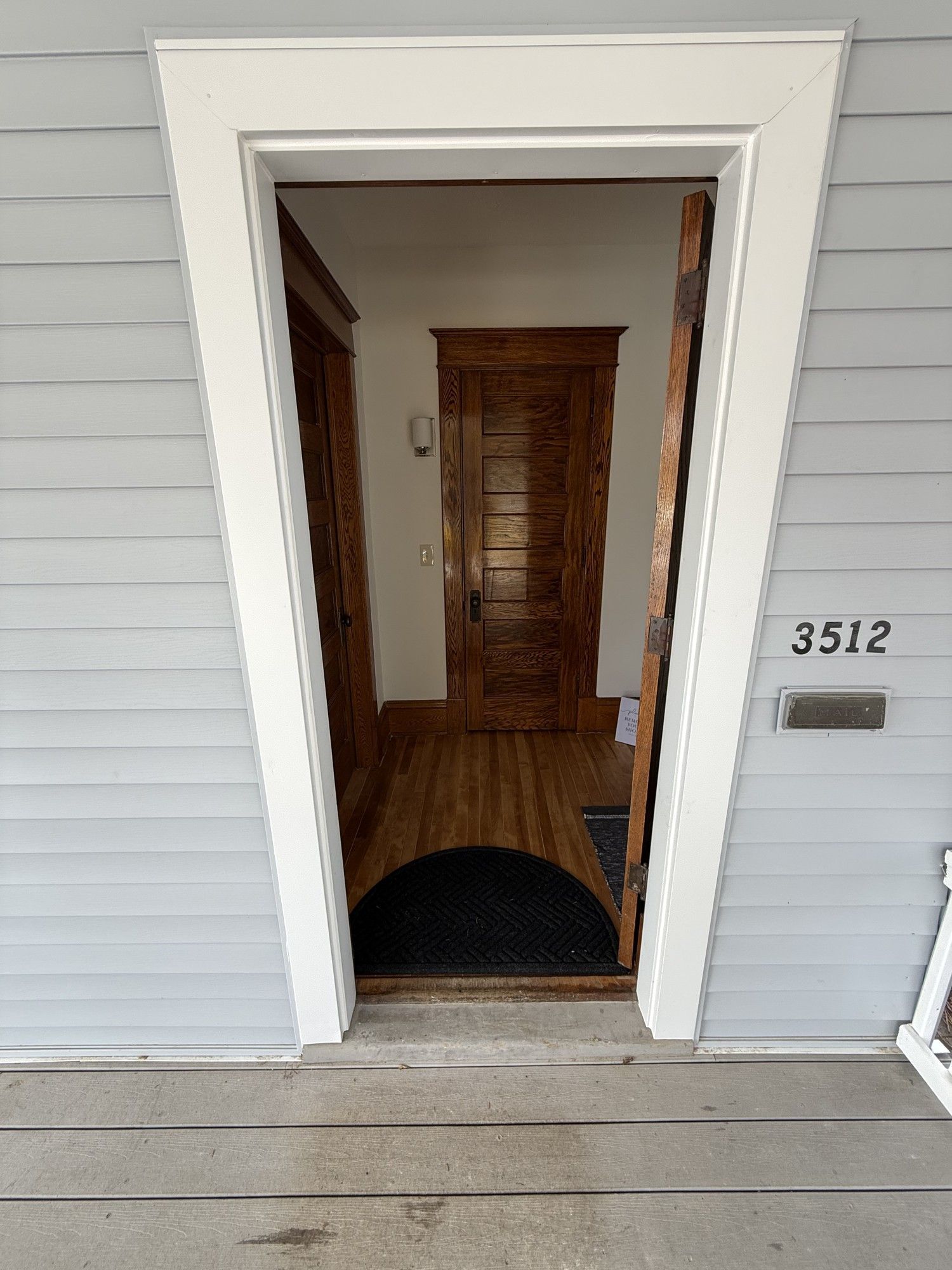 Open front doorway of a house with white siding, showing a wooden interior door and entry hall.