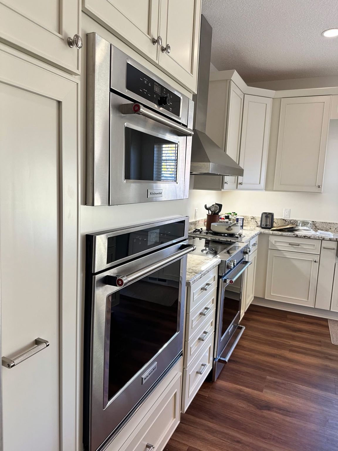 Bright white kitchen with built-in stainless steel oven, microwave, and wood floors along the counter.