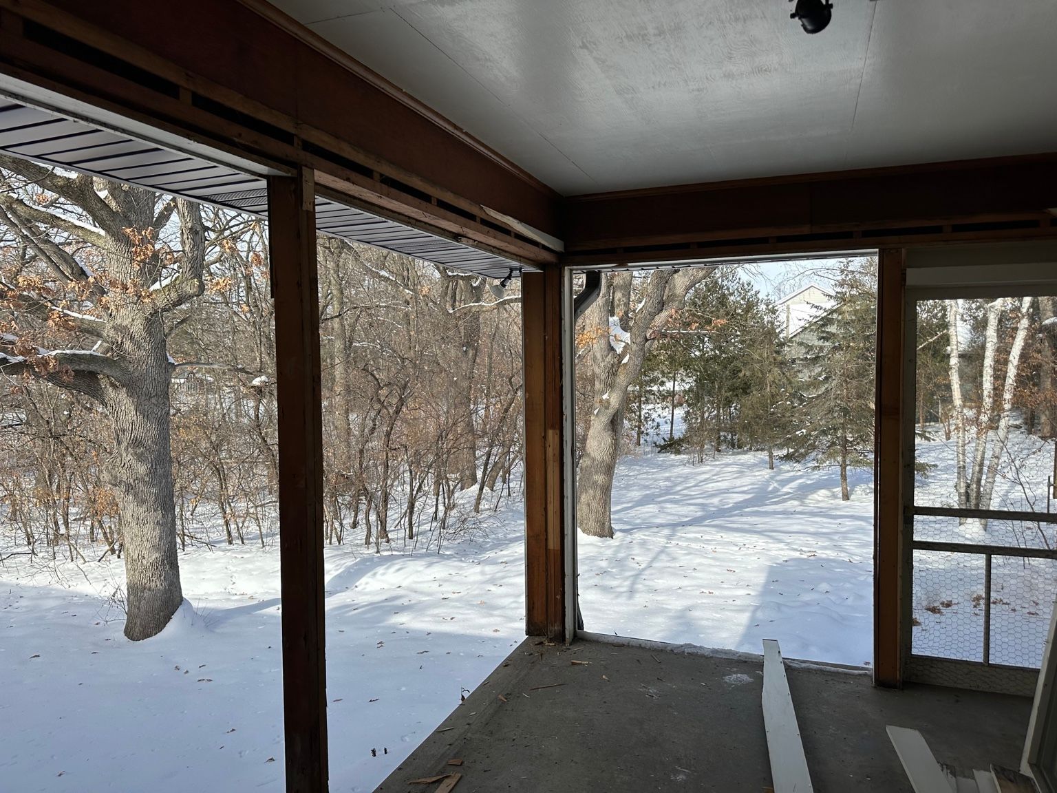 Covered porch overlooking a snowy yard with bare trees and a glass door on the right