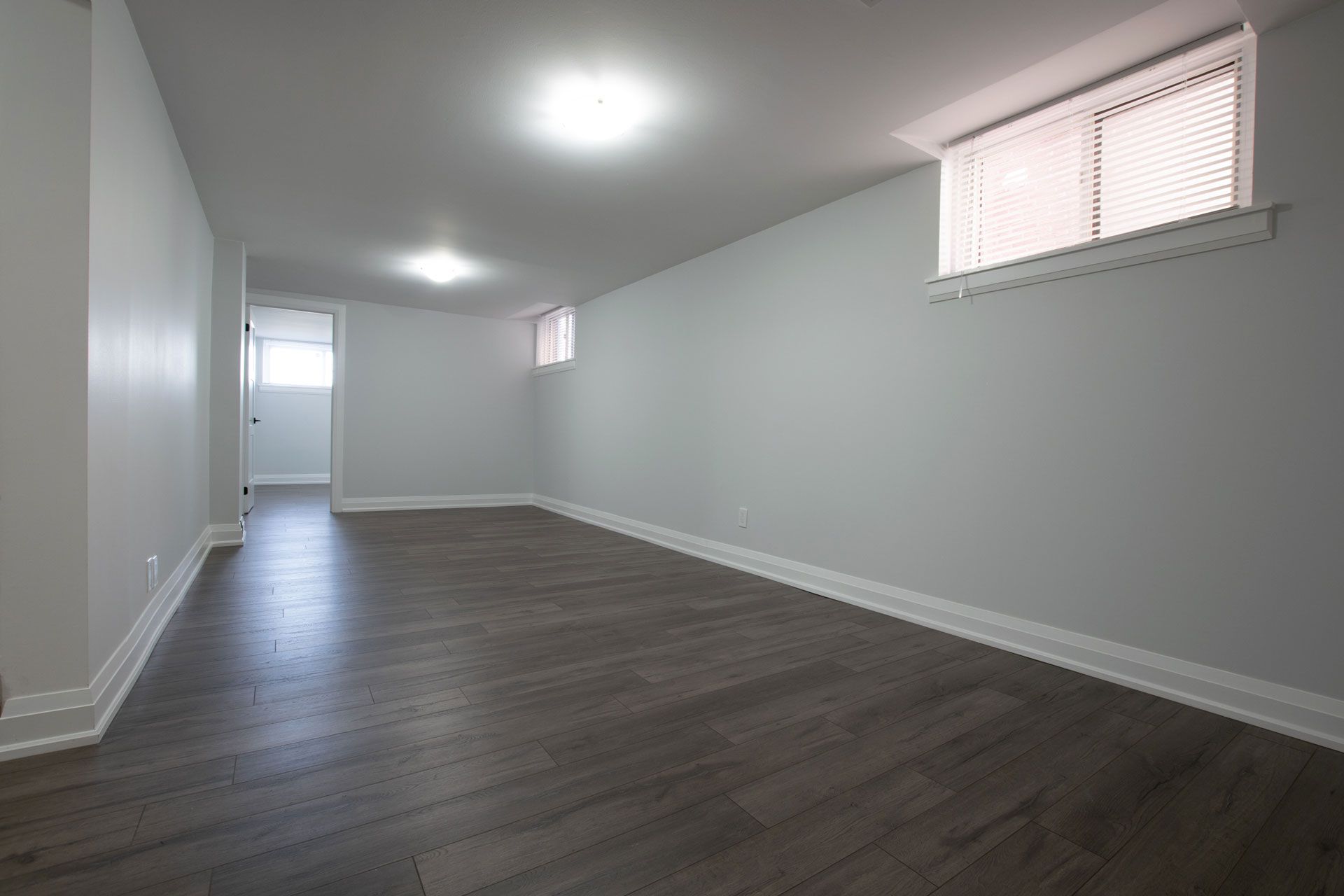 Empty modern room with gray walls, dark wood floor, and small high windows