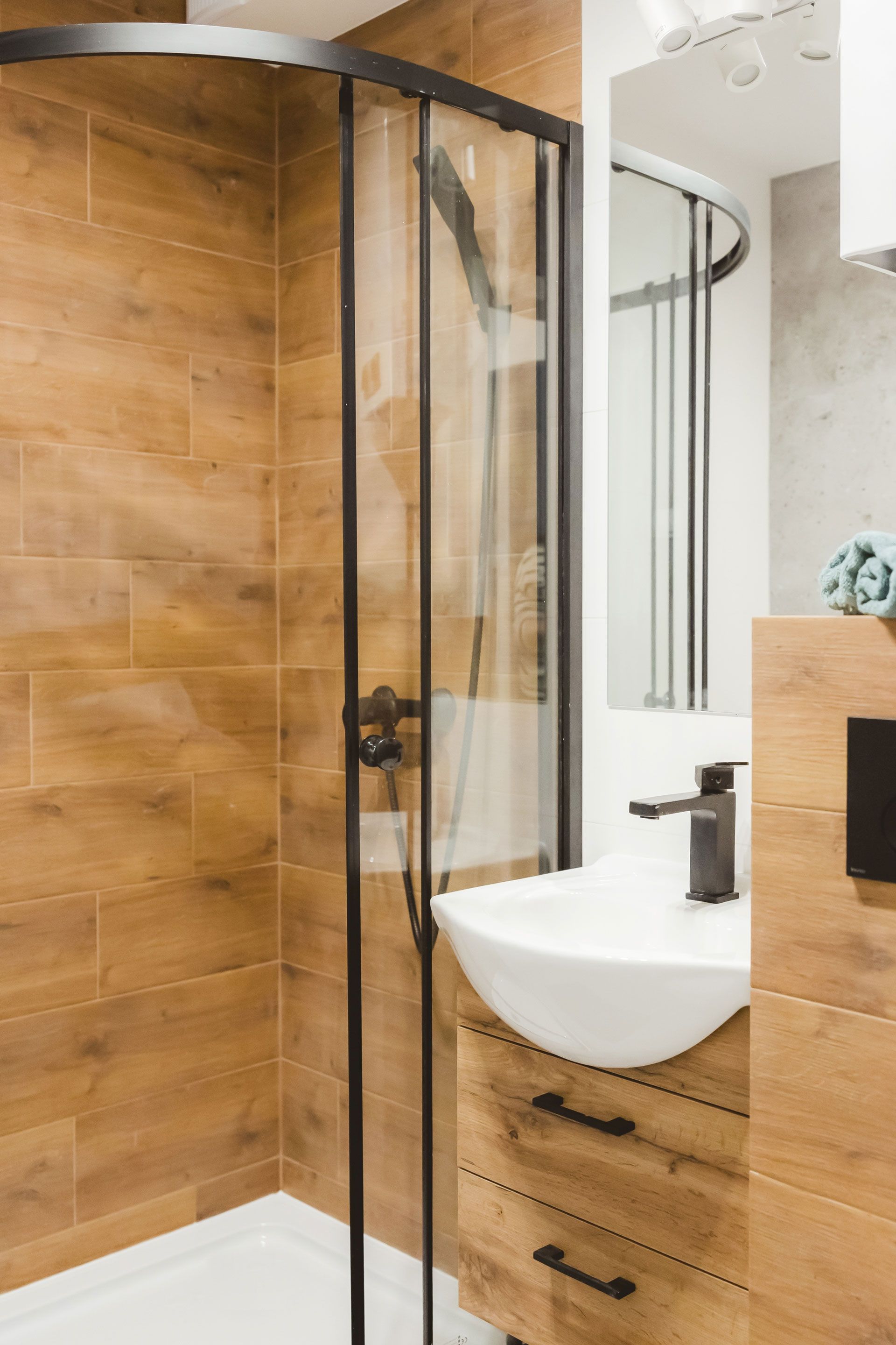 Modern bathroom with a curved glass shower, wood-paneled walls, and a white sink vanity