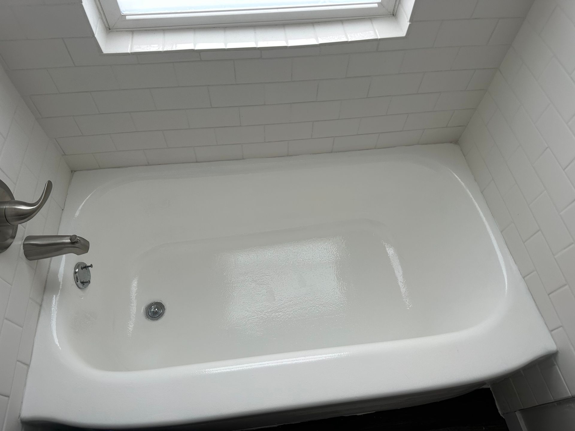 White bathtub under a small window in a bathroom.