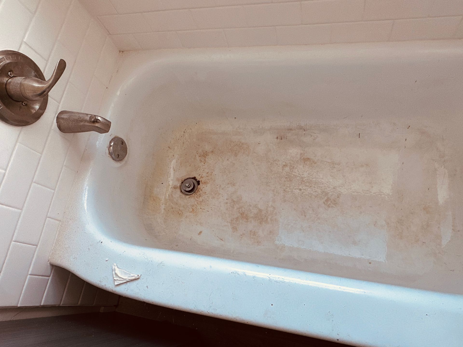 Dirty white bathtub with rust stains and a faucet in a tiled bathroom