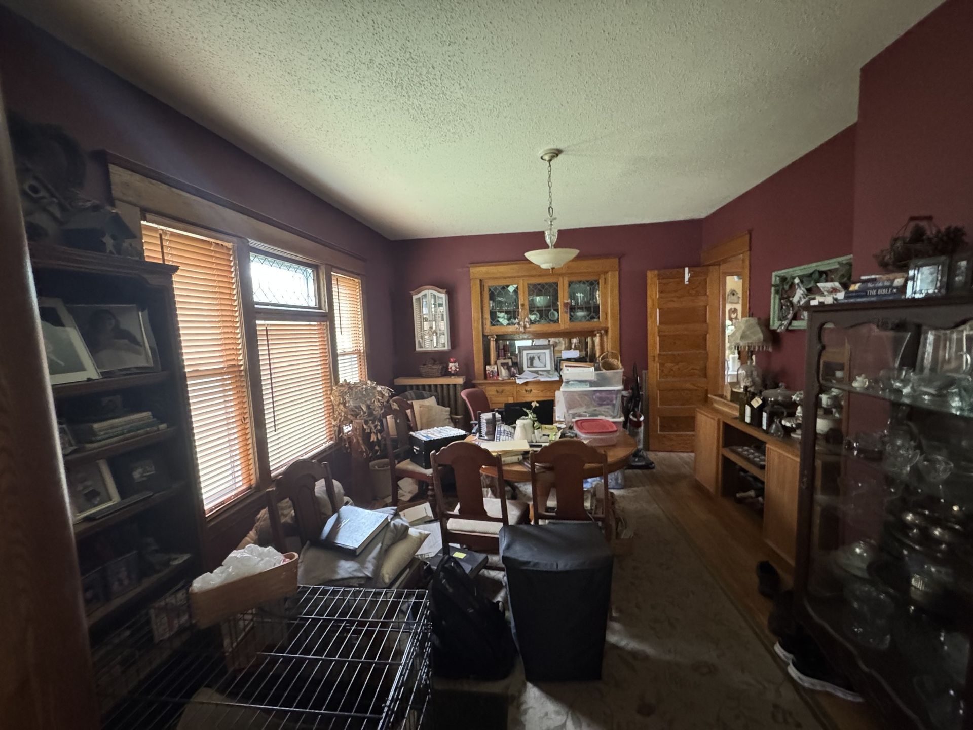 Cluttered living room with maroon walls, wood furniture, and a glass cabinet.