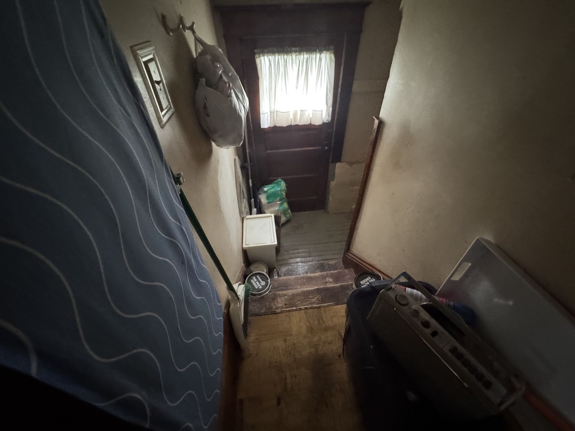 Narrow stairwell with a curtain, hanging items, and a door with light at the end.