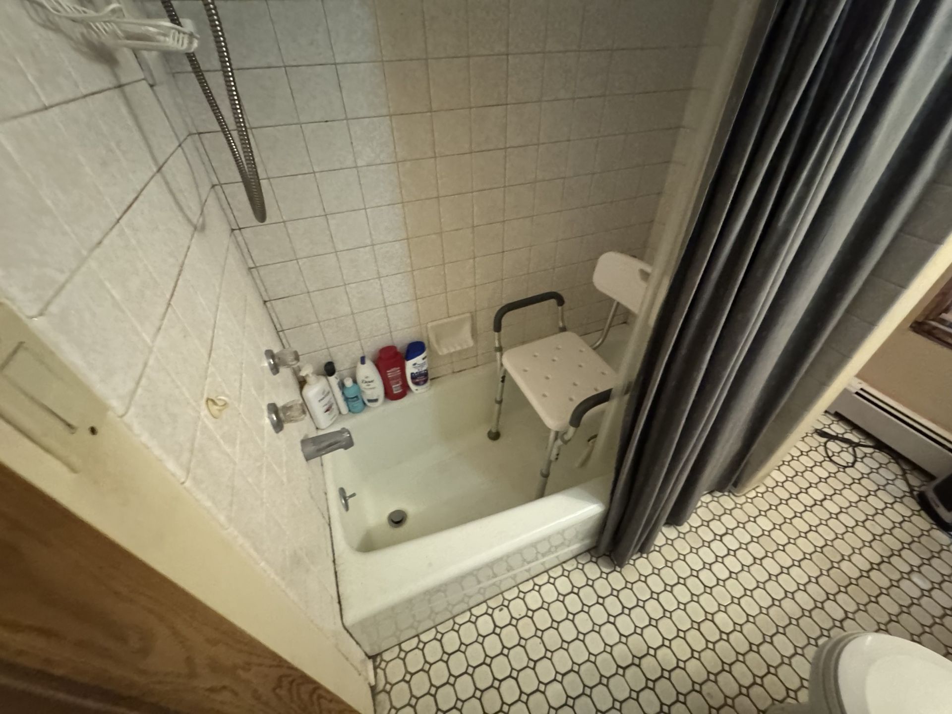 Small tiled bathroom with a bathtub, shower curtain, sink shelf, and hex tile floor.
