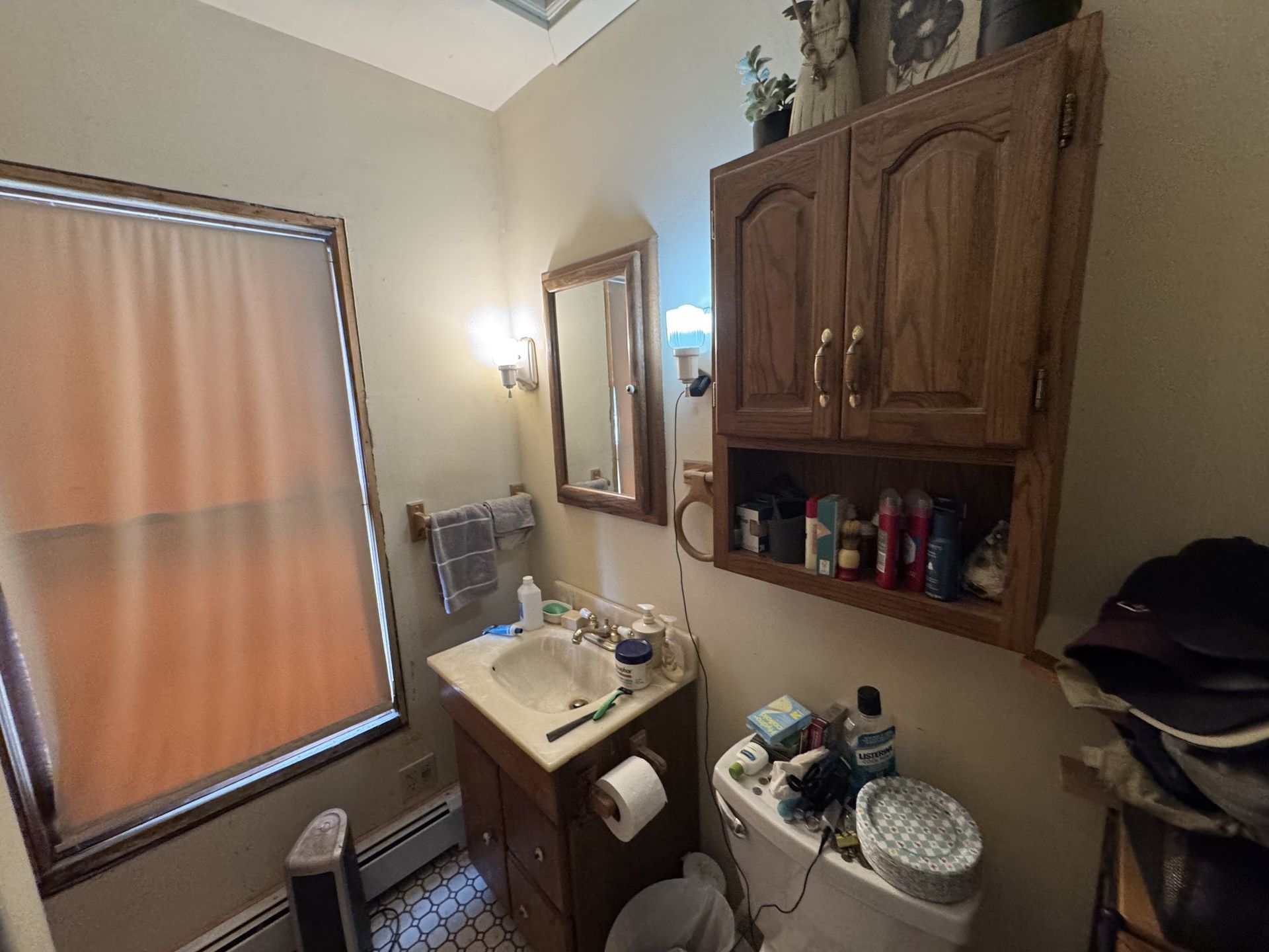 Small bathroom with sink, mirror, wall cabinet, toilet, and window covered by a beige blind.