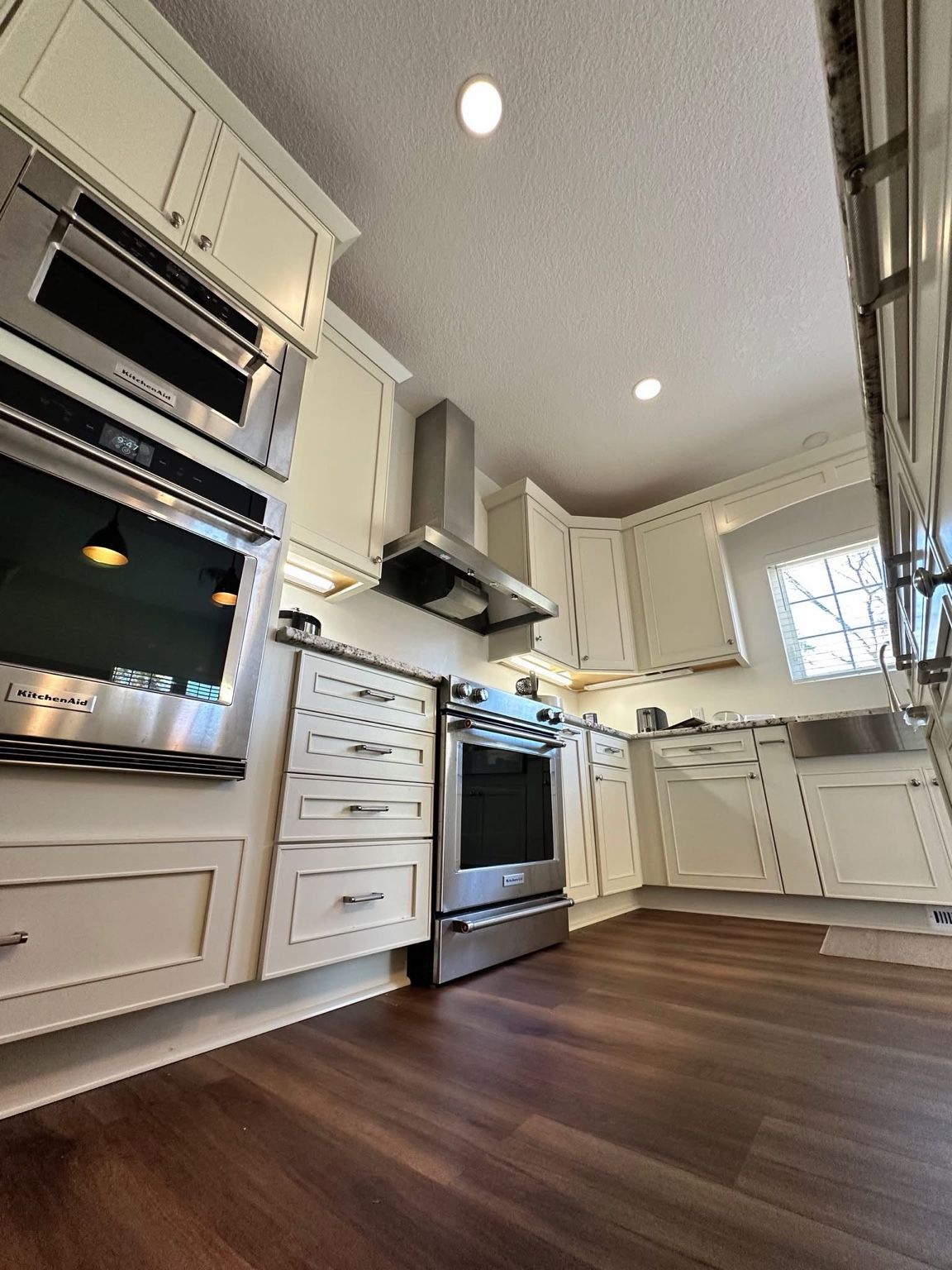 Bright kitchen with white cabinets, stainless steel appliances, and dark wood floors