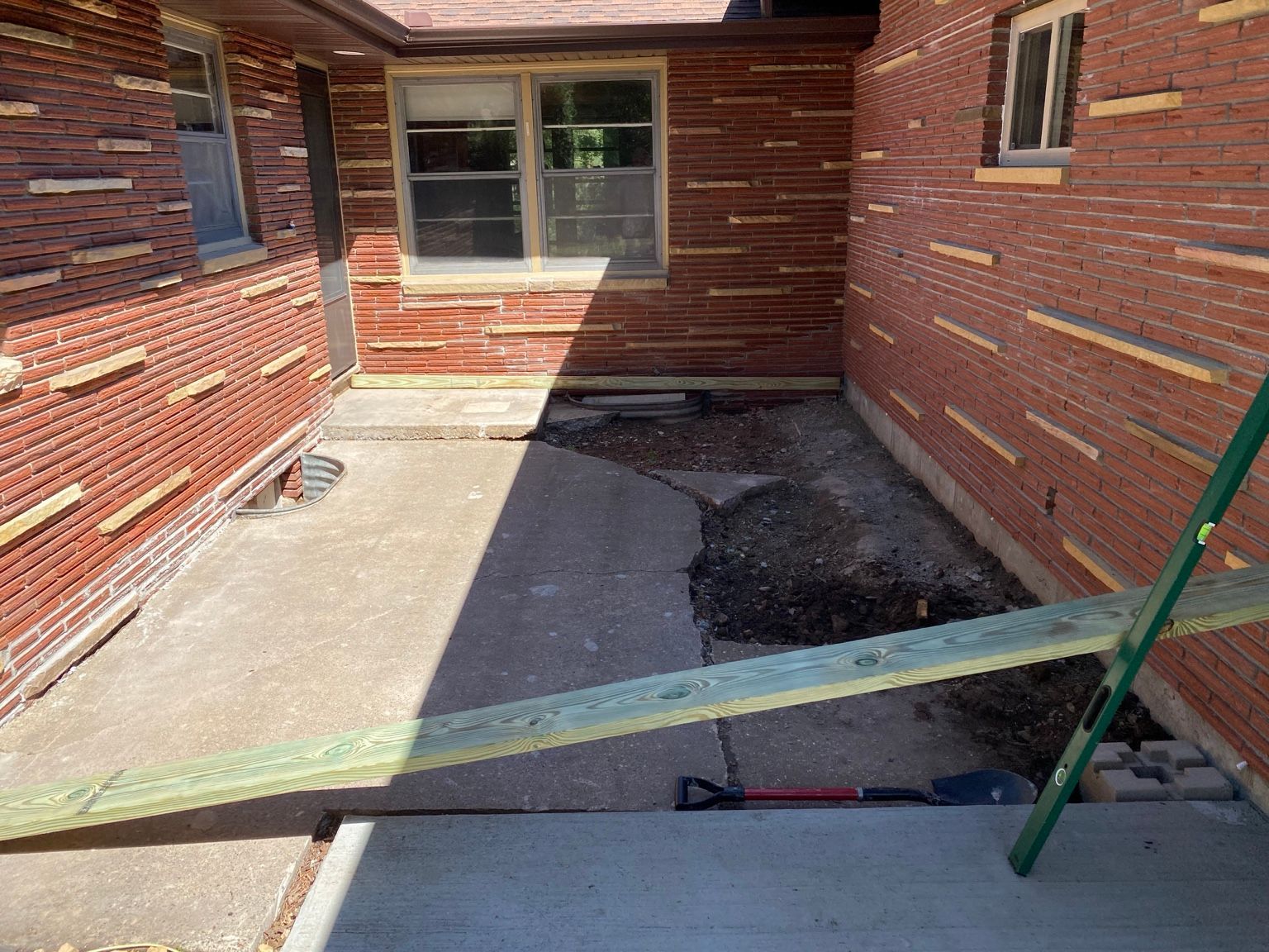Brick patio with a concrete walkway, window, and a hole covered by a board and green pole.