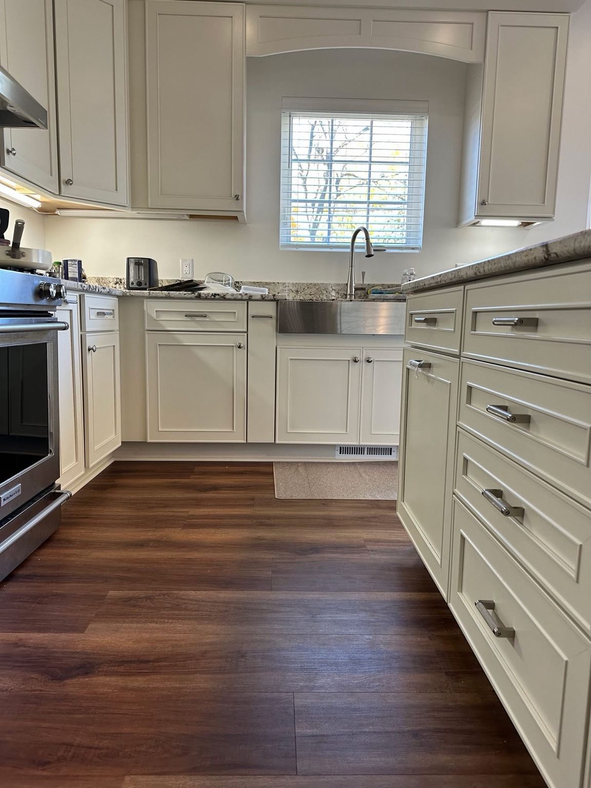 Bright white kitchen with wood floors, stainless steel sink, and window over the counter