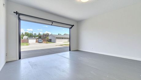 Empty modern garage with open door, gray floor, white walls, and a view of the street outside
