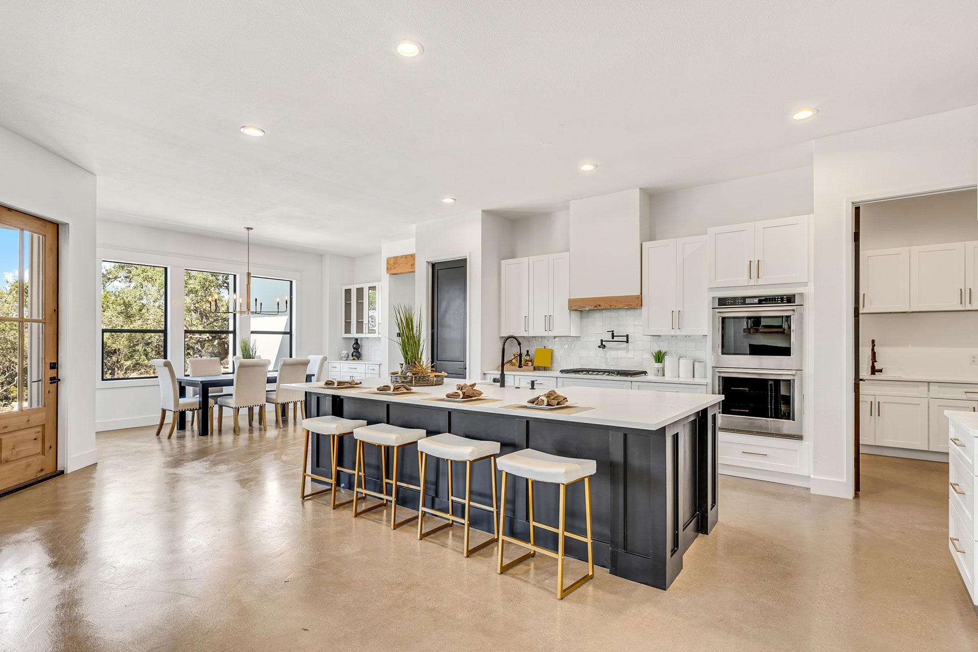 Bright modern kitchen with island, stools, white cabinets, and dining area with large windows