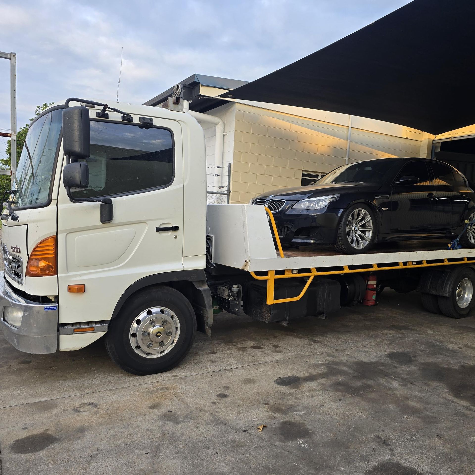White Tow Truck With Black Car on Its Flatbed, Under a Shaded Area — Old Mate's Towing Townsville in Deeragun, QLD