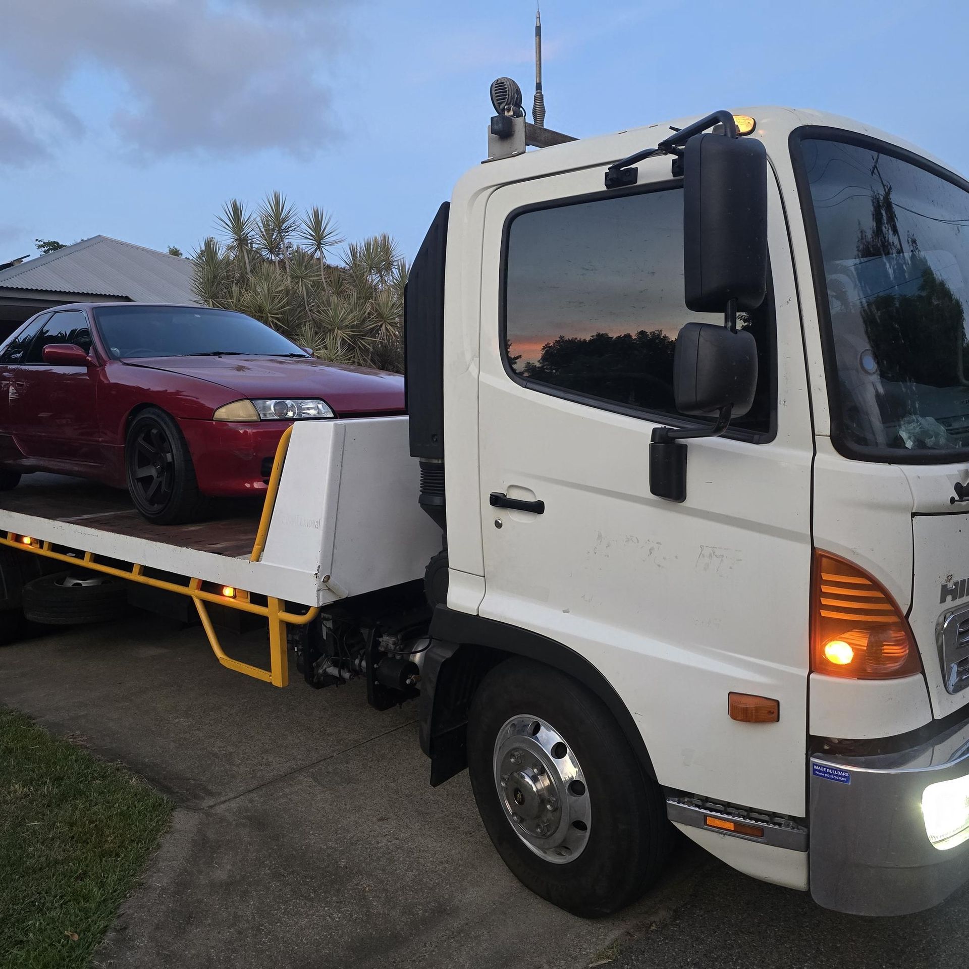 Red Car Loaded Onto a White Tow Truck at Dusk — Old Mate's Towing Townsville in Deeragun, QLD