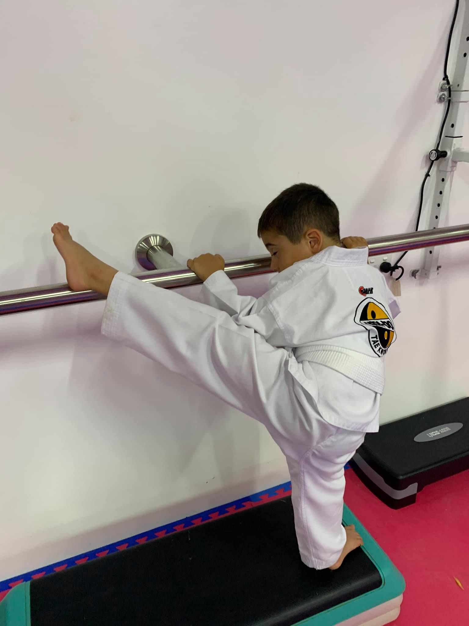 A Young Boy in a Karate Uniform is Doing a Split Against a Wall