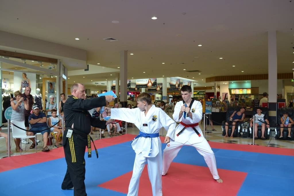 A Man Helping a Kid Train Punches With a Wooden Board — Him-Do Tae Kwon Do Academy In Salamander Bay, NSW